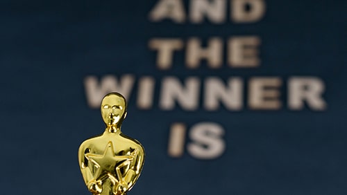 Plastic Oscar award and blurred wooden letters with the phrase "And the winner is" on black background