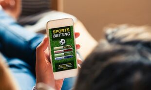 Man laying on a couch holding his mobile phone with sports betting app open