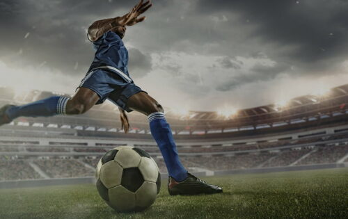 Save Download Preview Professional football or soccer player in action on stadium with flashlights, kicking ball for winning goal