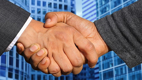 Zoomed photo of hands shaking against a background of business buildings