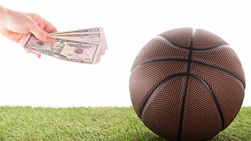 Hand handing out dollars beside a ball. Concept of sports gambling