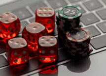 Online casino concept. Gambling chips and five red dices on laptop keyboard close-up