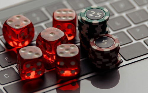 Online casino concept. Gambling chips and five red dices on laptop keyboard close-up