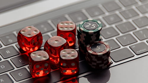 Online casino concept. Gambling chips and five red dices on laptop keyboard close-up