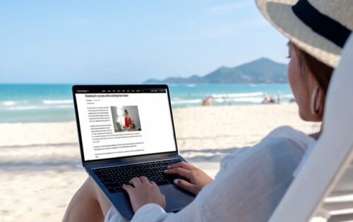 Mockup image of a woman using and typing on laptop computer in the beach