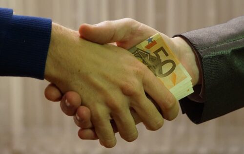 Two men shaking hands with money in between their hands