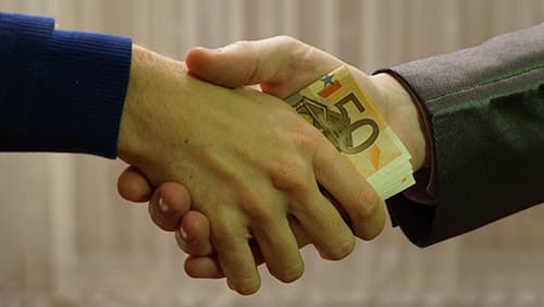 Two men shaking hands with money in between their hands