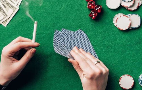 Woman holding cigarette and playing cards by casino table