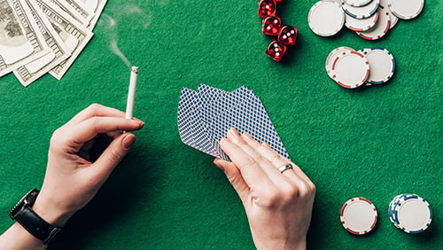 Woman holding cigarette and playing cards by casino table