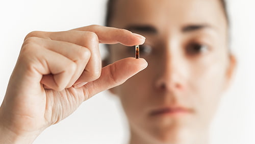 Person holding in fingers micro chip for implantation with defocused face on background