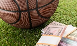 Close-up view of basketball ball near dollar and euro banknotes on green grass, sports betting concept