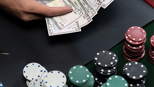 Close up of a poker table with chips and a hand holding cash