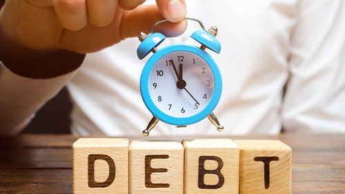 Wooden blocks with the word Debt and the clock in the hands of a businessman