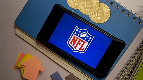NFL logo on a mobile screen with bitcoins signifying digital currencies