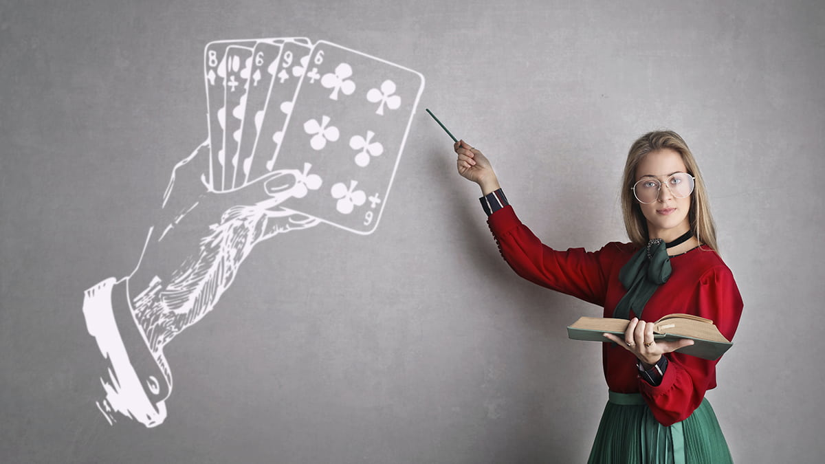 A teacher pointing a drawing of playing cards and a hand on a blackboard