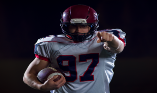 portrait-of-confident-american-football-player-holding-ball-while-standing-on-field-at-night