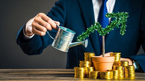 A business man watering a plant with gold coins on its side. Investment concept.