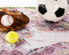 baseball glove and ball, soccer, tennis and rugby balls near betting lists