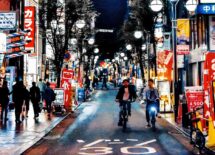 People riding the bike and walking on the side walk, night life, Japan city at night