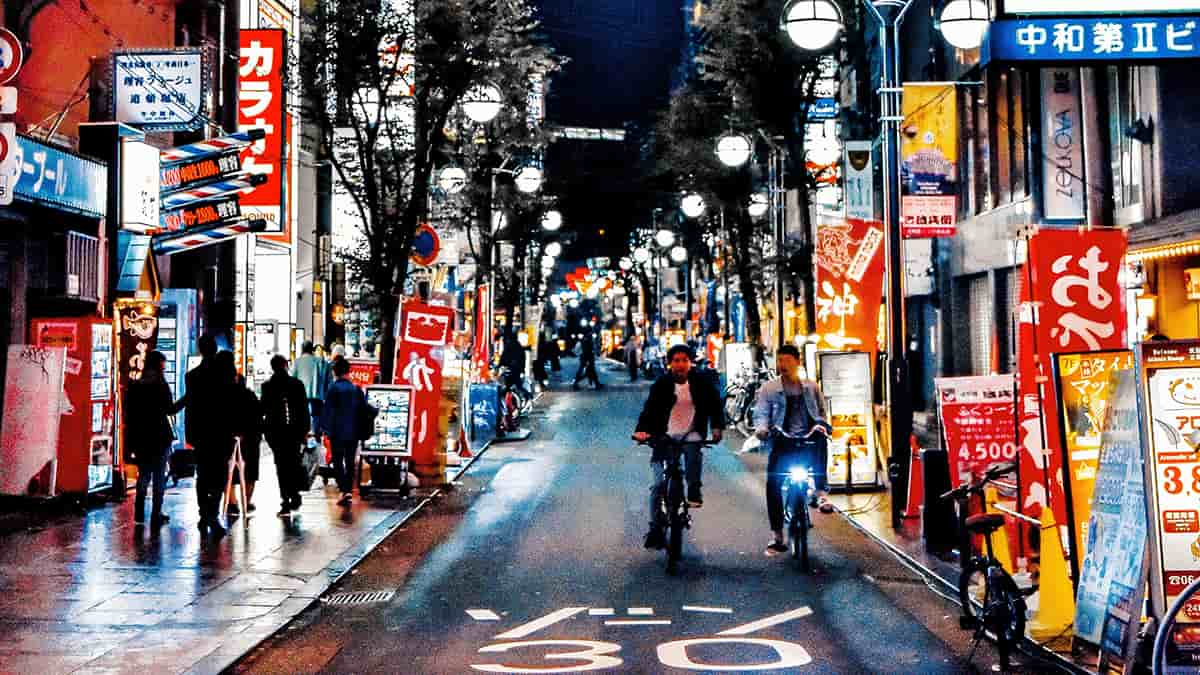 People riding the bike and walking on the side walk, night life, Japan city at night