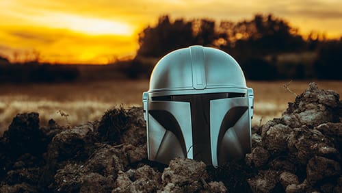 Mandalorian helmet on the ground with a sunset background