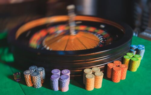 A close-up vibrant image of multicolored casino table with roulette in motion with the hand of croupier and a group of gambling rich wealthy people in the background