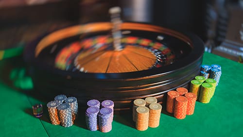 A close-up vibrant image of multicolored casino table with roulette in motion with the hand of croupier and a group of gambling rich wealthy people in the background